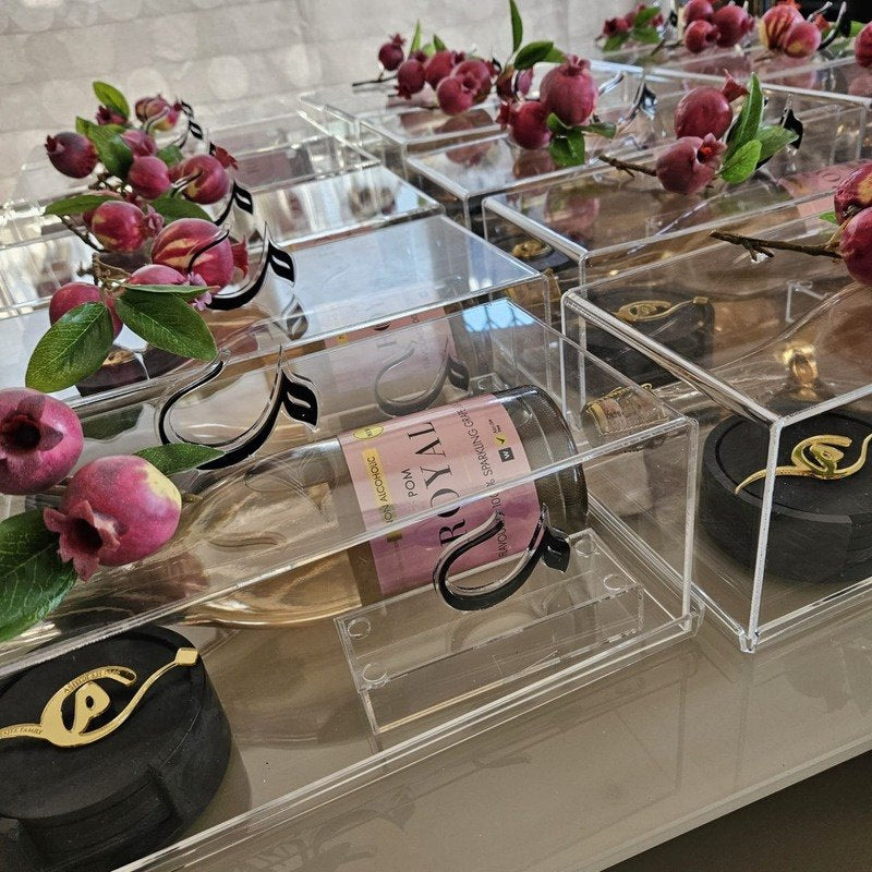 Curated gift boxes in clear perspex with a sparkling drink, pomegranates and gold-detailed coasters